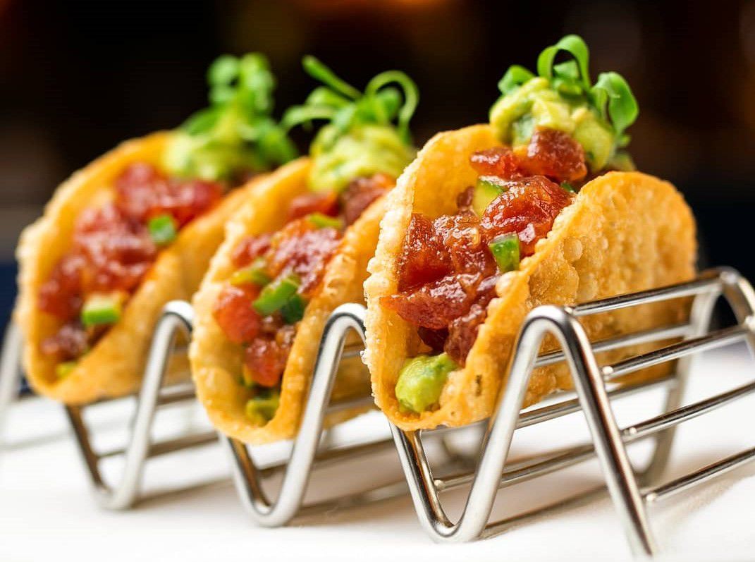 A metal rack filled with three tacos stuffed with tuna and green garnishes.
