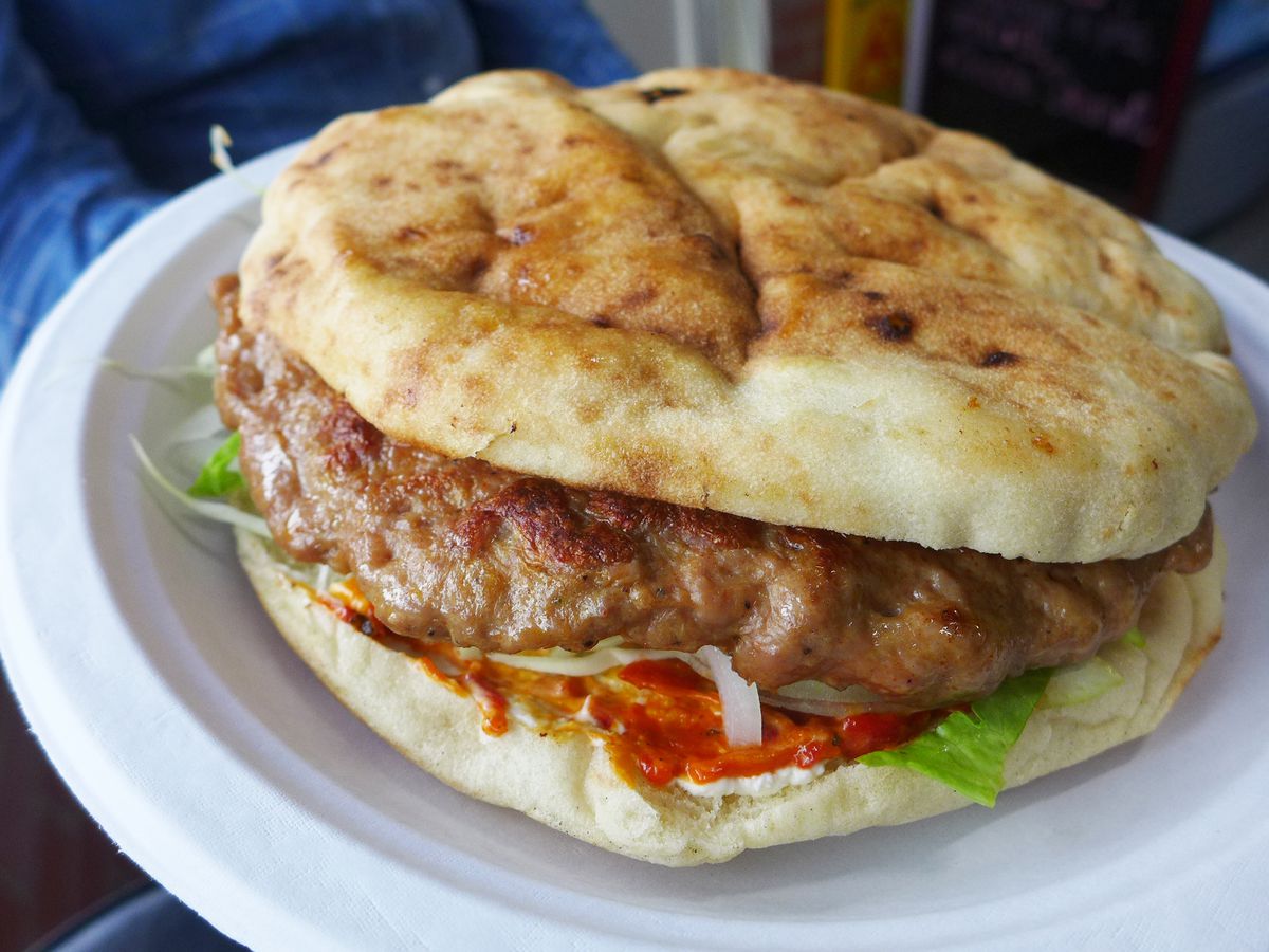 A burger in a mottled and irregular bun with some angry looking red sauce visible on the bottom half of the bun, lettuce, too.