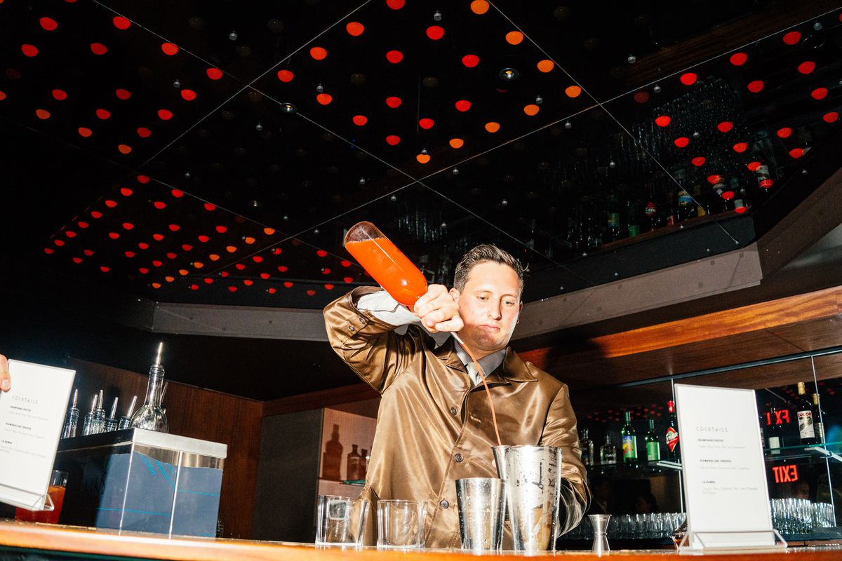 A bartender pours a red mixer into a stainless steel container.