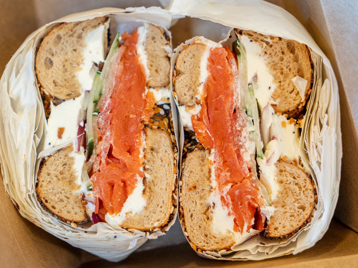 Two halves of lox bagel with onion, tomato, and cream cheese in 