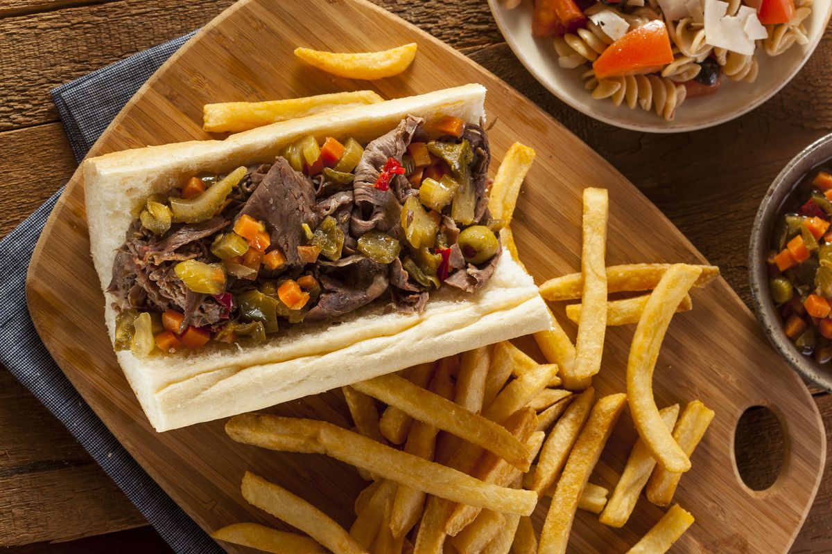 An Italian beef sandwich and fries on a wooden board