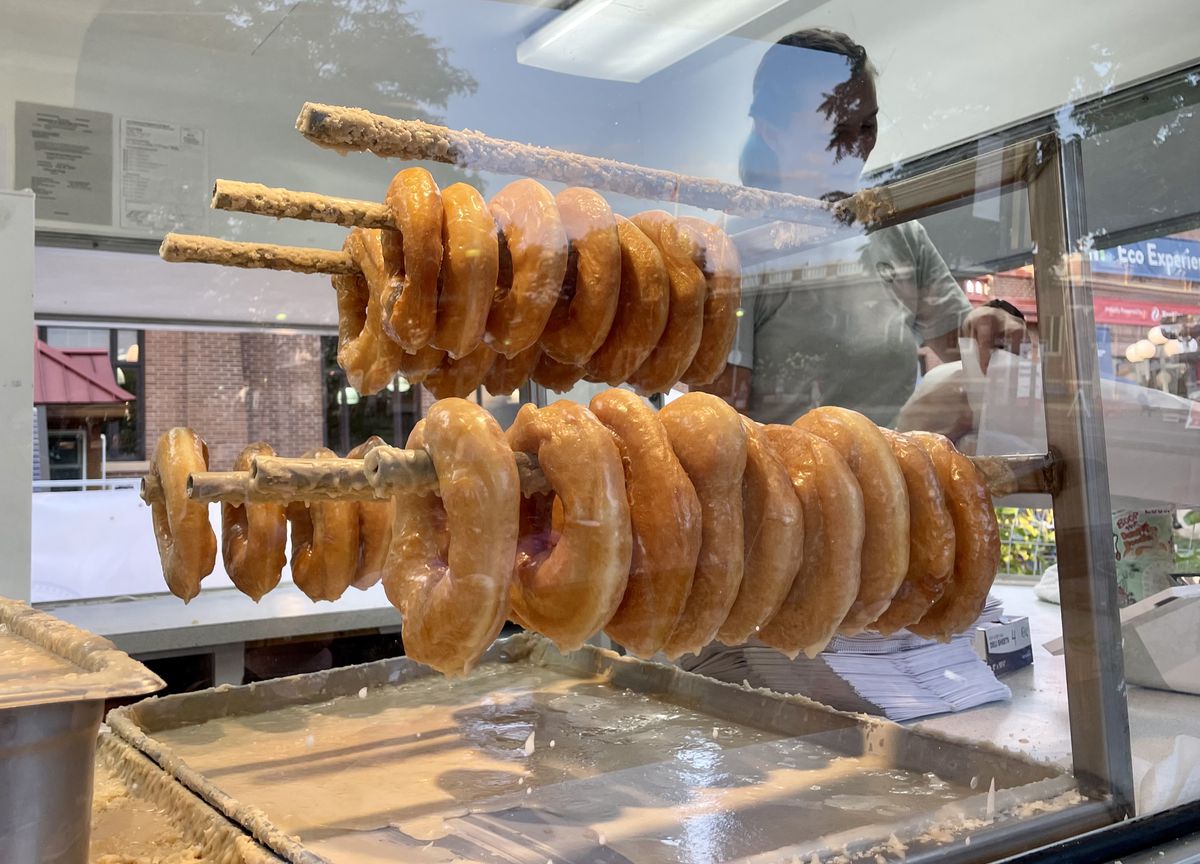 Racks of glazed doughnuts behind a glass pane. 
