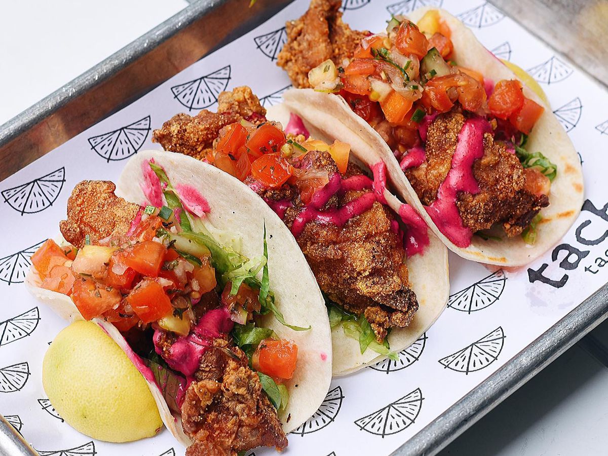 Three fried fish tacos on patterned branded paper in a sheet pan.