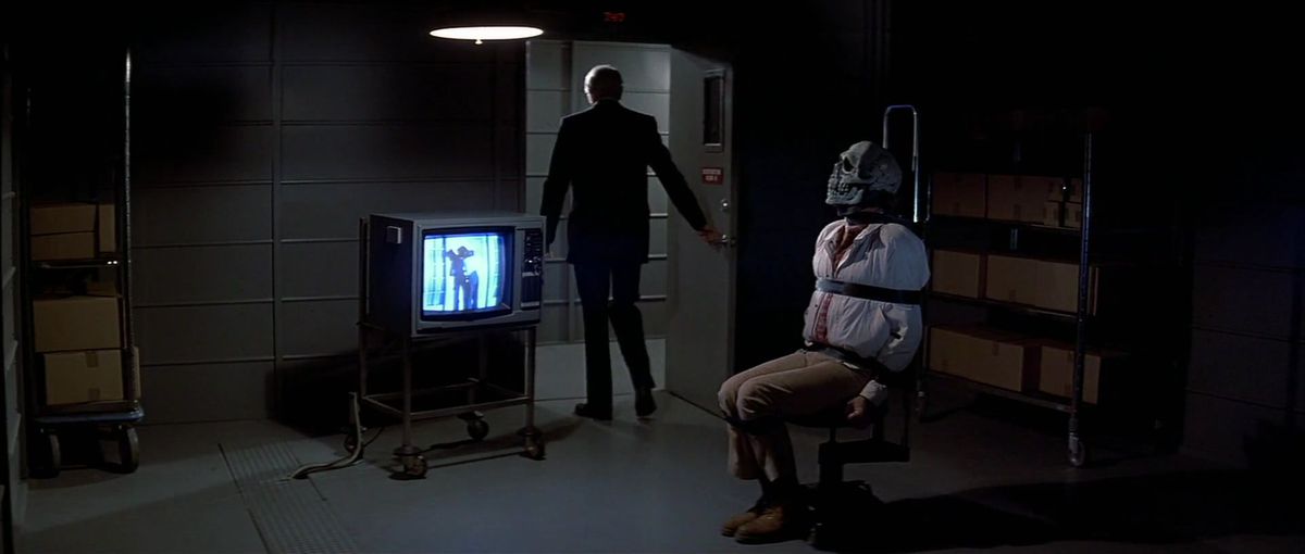 Un hombre atado a una silla con una máscara de calavera se ve obligado a mirar televisión en Halloween III: Season of the Witch.