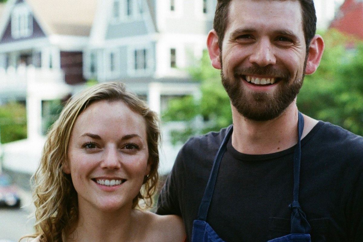 A young woman and man stand next to each other smiling for an outdoor, daytime photo with houses visible in the background.