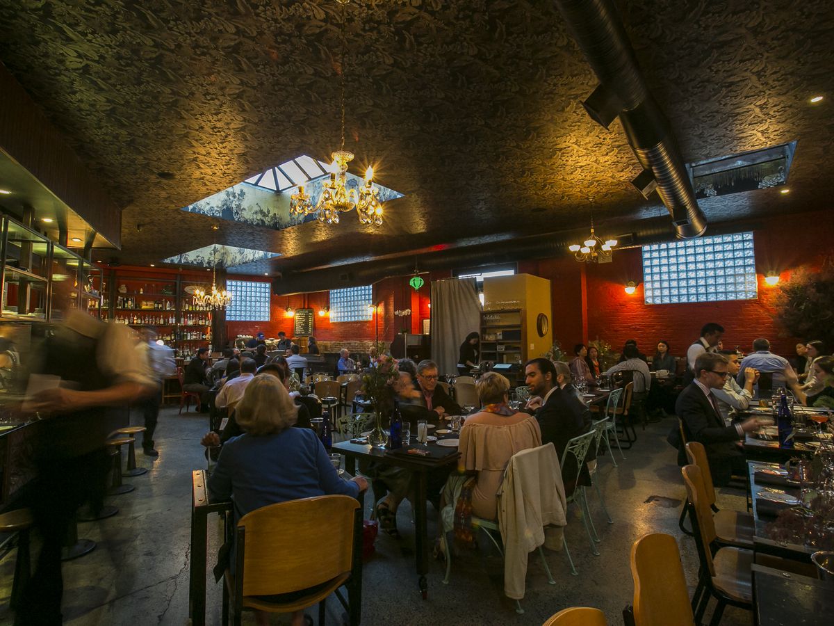 Customers are seated at tables in a high-ceilinged dining room at M. Wells, a restaurant in Long Island City. 