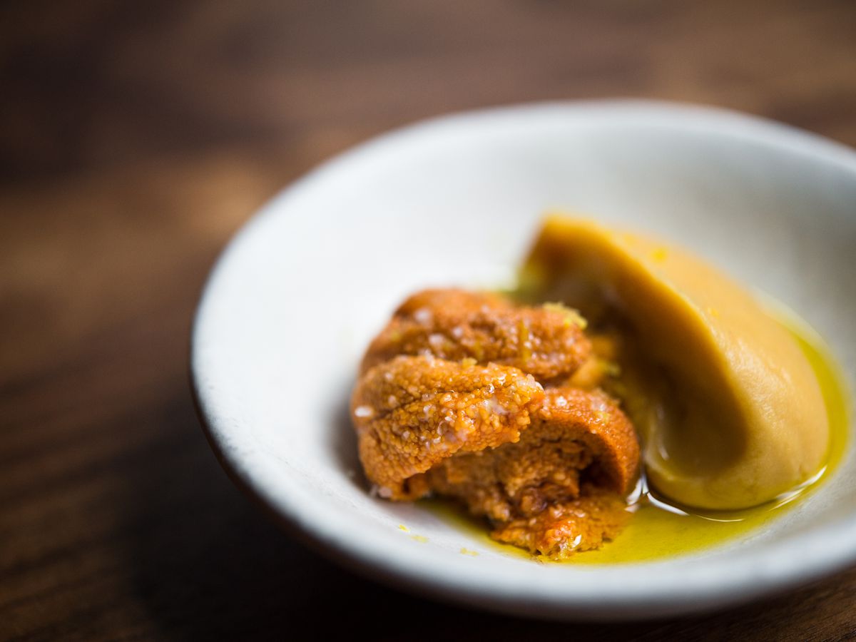 A few tongues of orange uni sit next to a yellow chickpea puree in a pool of green olive oil