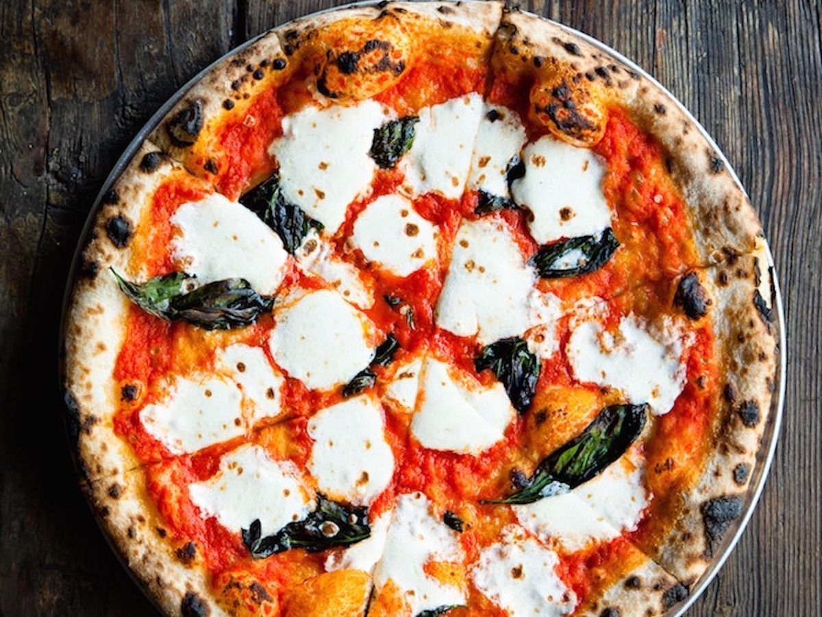 A top-down view of a whole pizza with a nicely charred crust covered in red sauce, fresh mozzarella, crisped basil leaves.