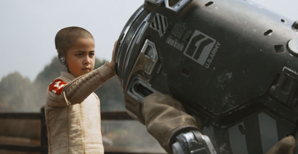 A young android child with a shaved head and partially missing skull places their hand on a piece of machinery in The Creator