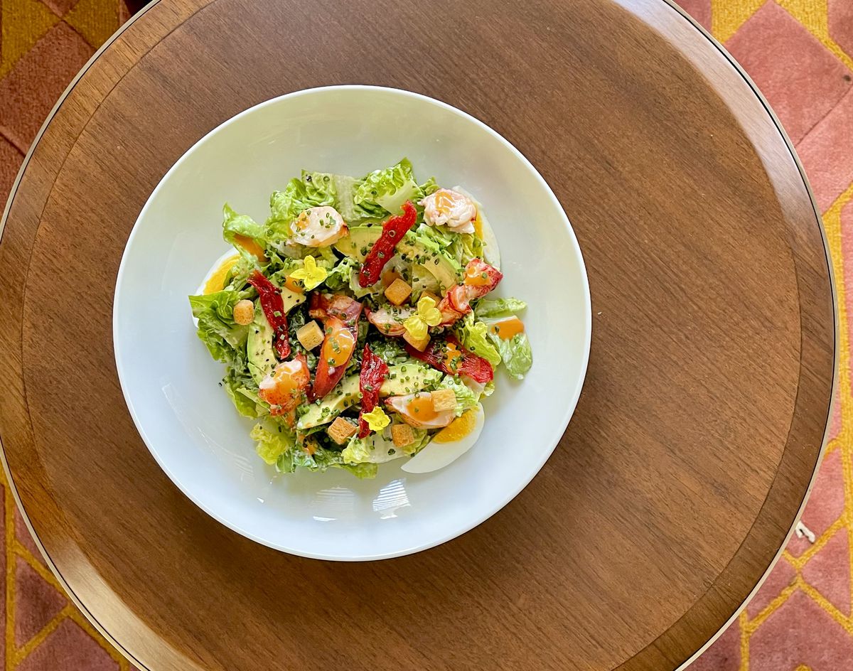 An overhead shot of a seafood salad with bright greens on a white circular table.