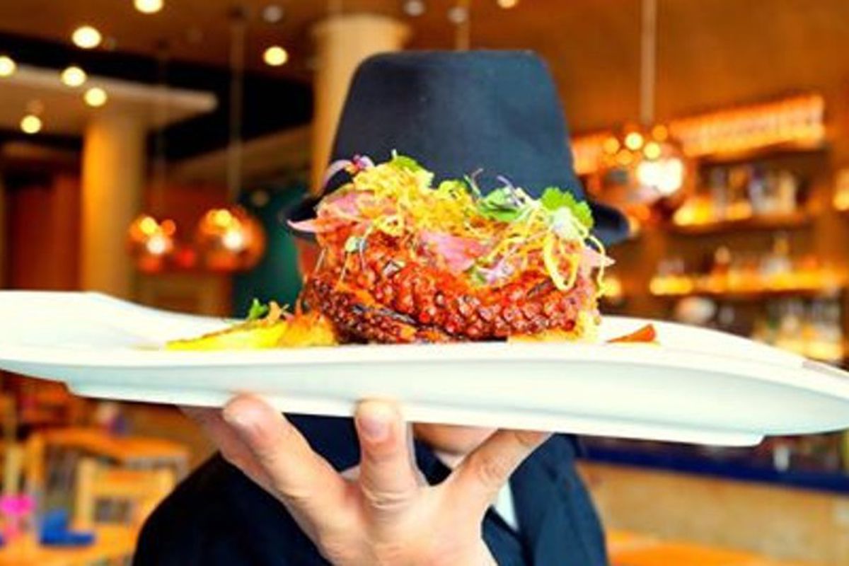 A man holds up a dish of grilled octopus.