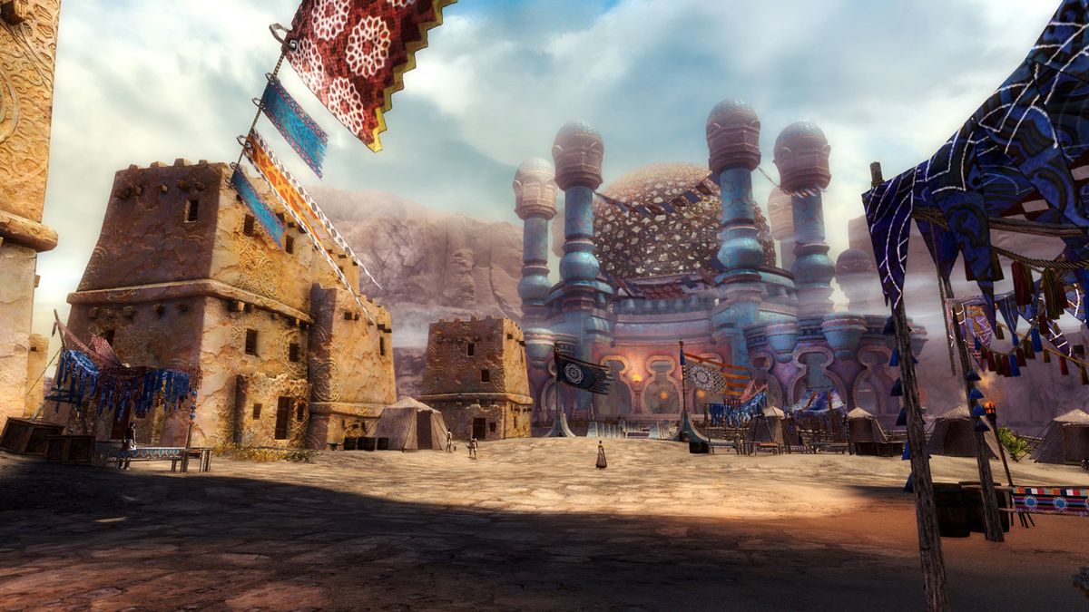 This screenshot from Guild Wars 2: Path of Fire shows the middle of a desert town. Adobe houses line the streets and an ornate palace can be seen on the opposite end with brightly-colored flags and banners flying nearby. A few people are in the dusty stre