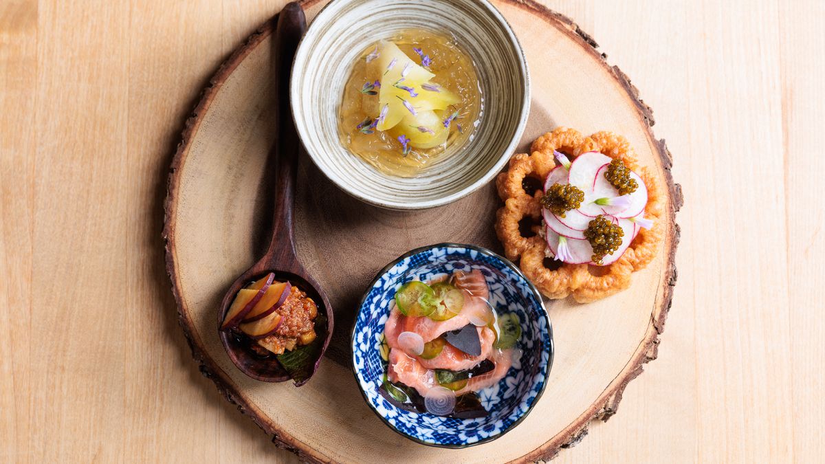 Pea gelee, rosettes with chickpea miso and butter, rainbow trout, and red fish ‘nduja all sit in separate ramekins on a round wooden platter