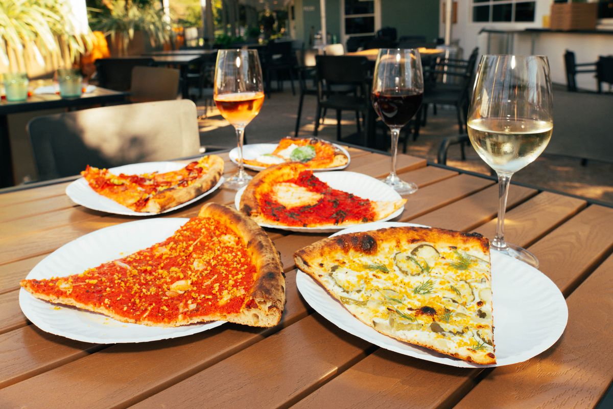 Slices of pizza on paper plates with glasses of wine.