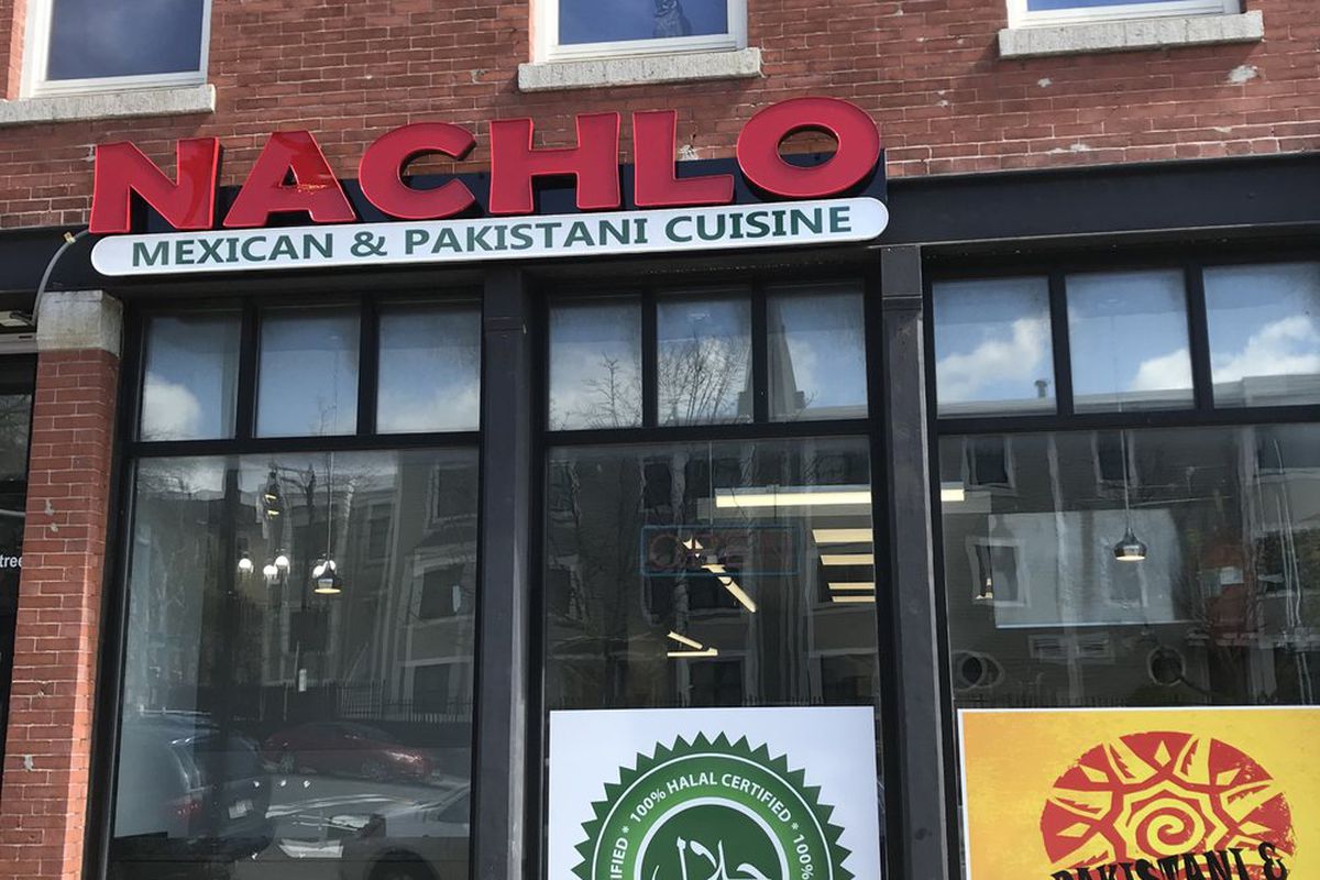 A casual restaurant exterior on the ground floor of a brick building has signage that reads “Nachlo: Mexican &amp; Pakistani Cuisine.” There’s also halal signage.