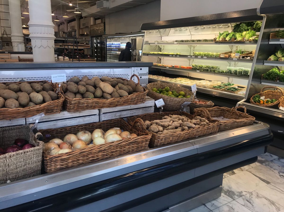 A few baskets of potatoes and onions inside a grocery store, though the back produce shelves are nearly empty