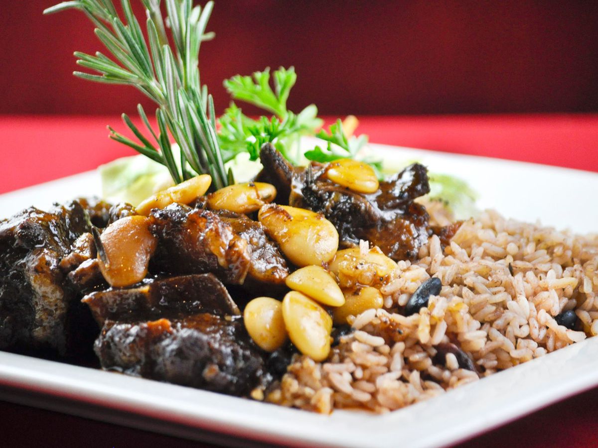 A white platter with braised oxtails, sprig of rosemary, vegetables, seasoned rice, and peas