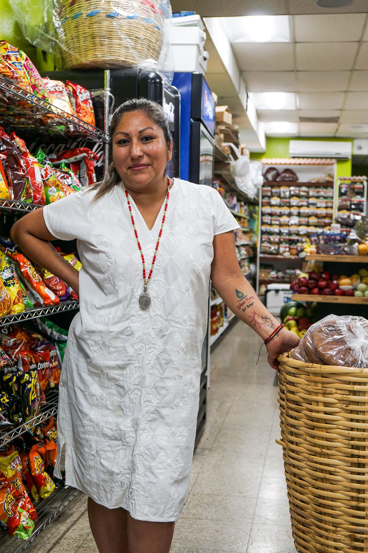 A Oaxacan woman wears a white gown a stands inside her store.