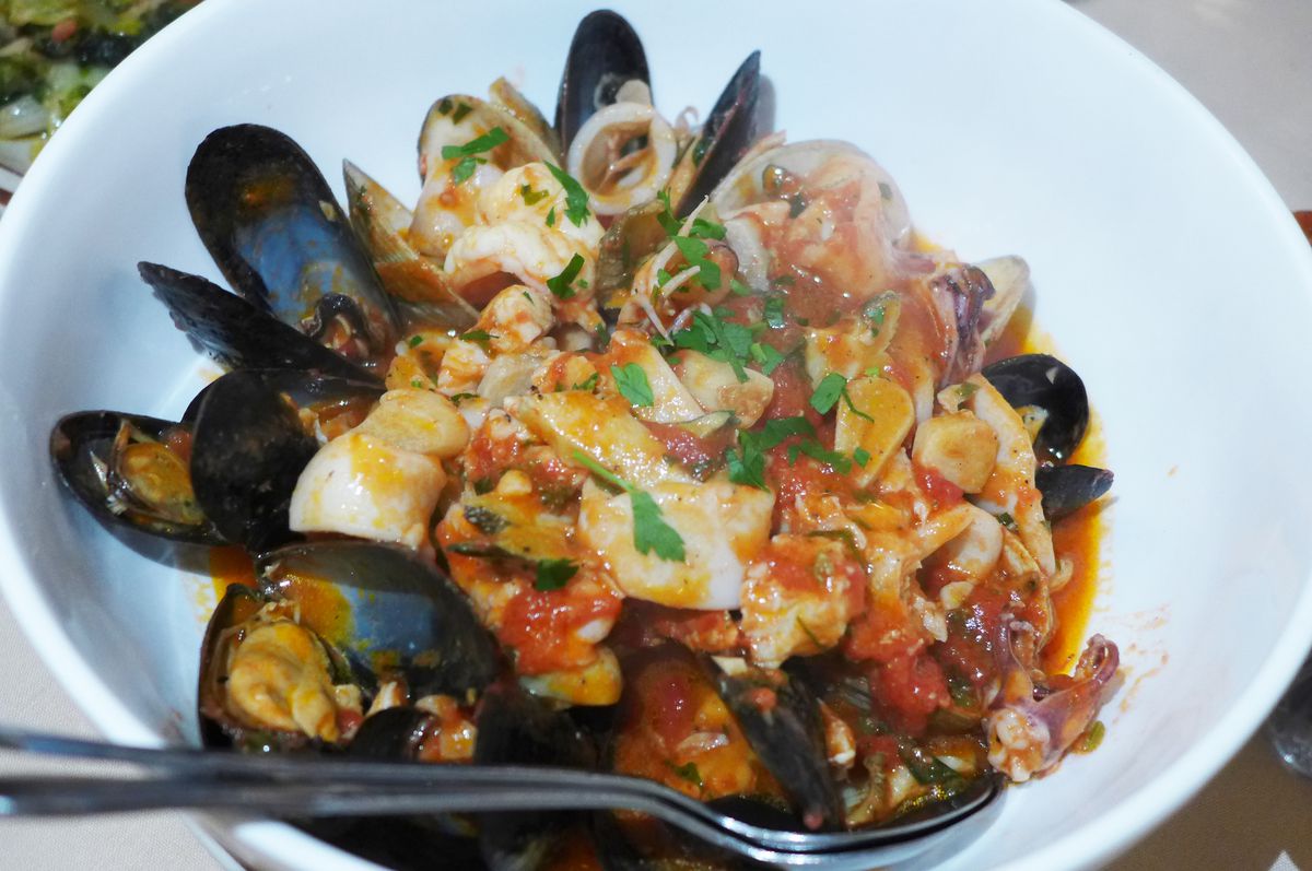 A white bowl filled with seafood including shellfish in a red sauce.