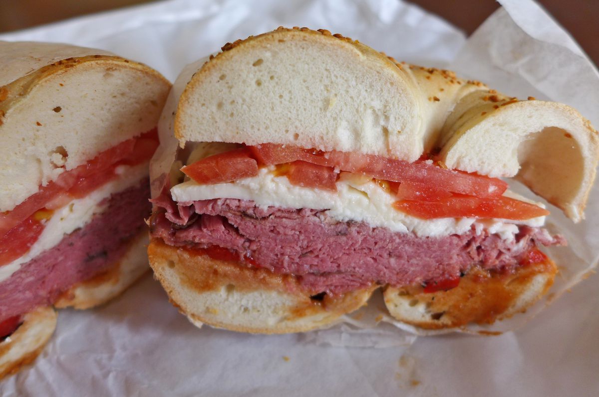 A bagel with roast beef and tomato on it, cut in half.