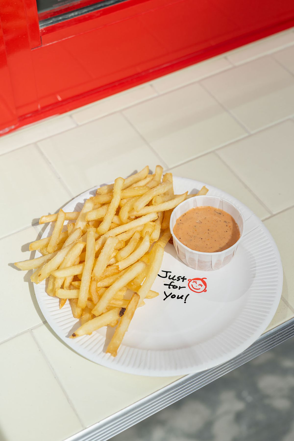 A pile of fries and a cup of orange sauce on a white paper plate.