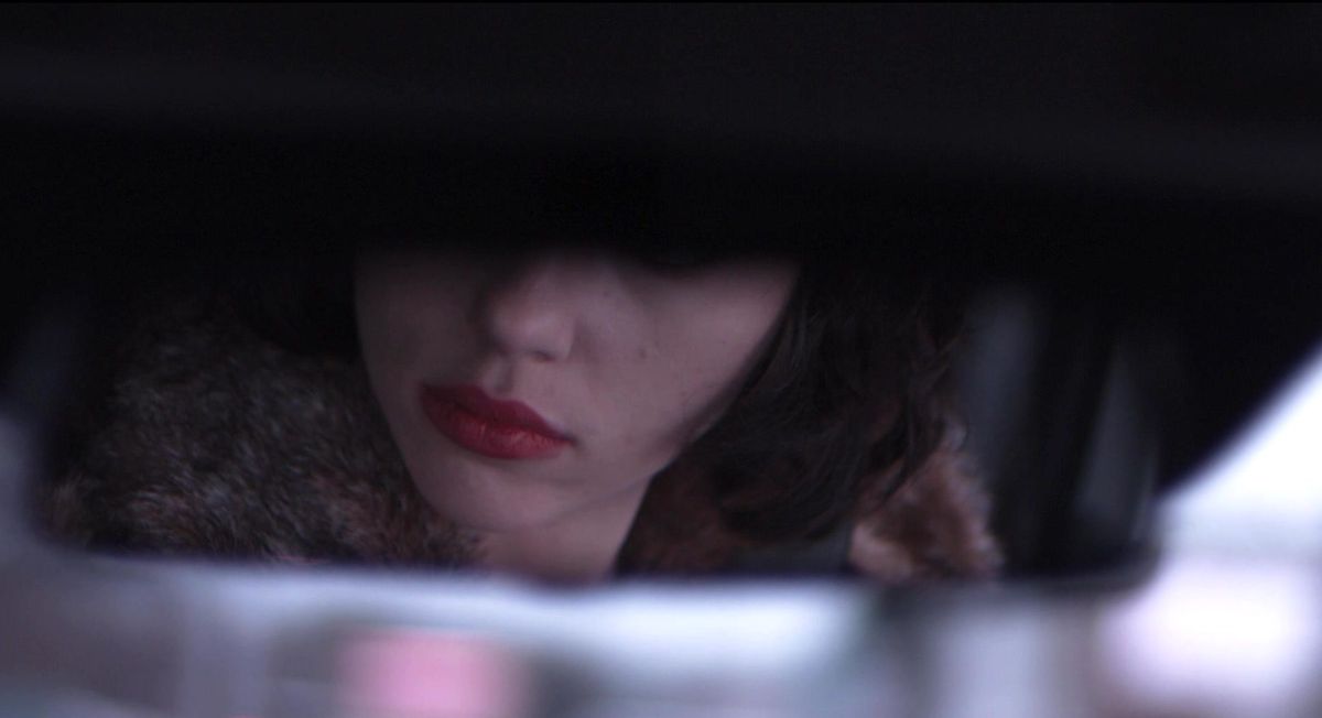 A rear-view mirror shows the lower half of Scarlett Johansson’s face in Under the Skin
