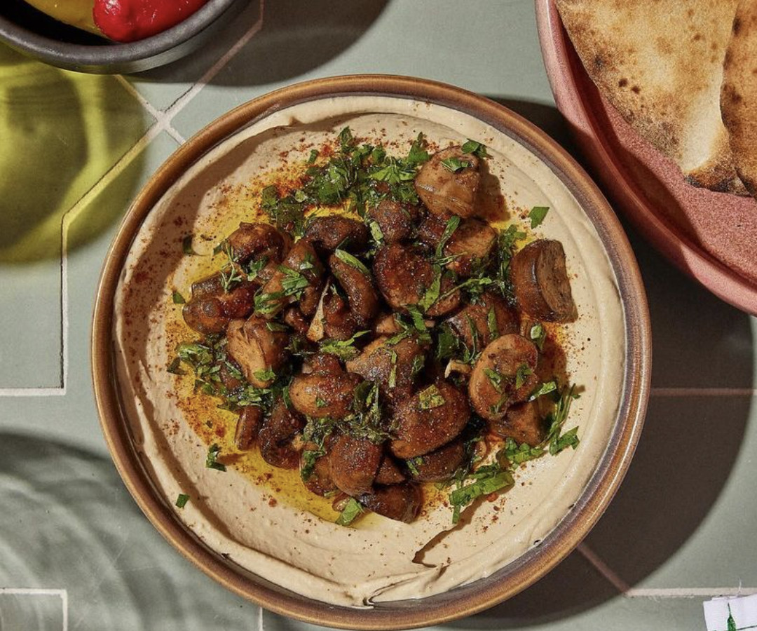 A hummus dish topped with meat and herbs.