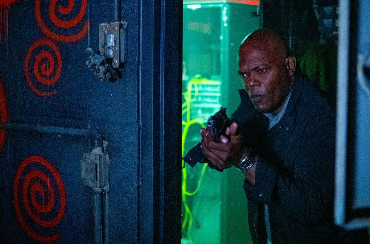 Samuel L. Jackson, gun drawn, looks into a room with red spray-painted spirals on the walls