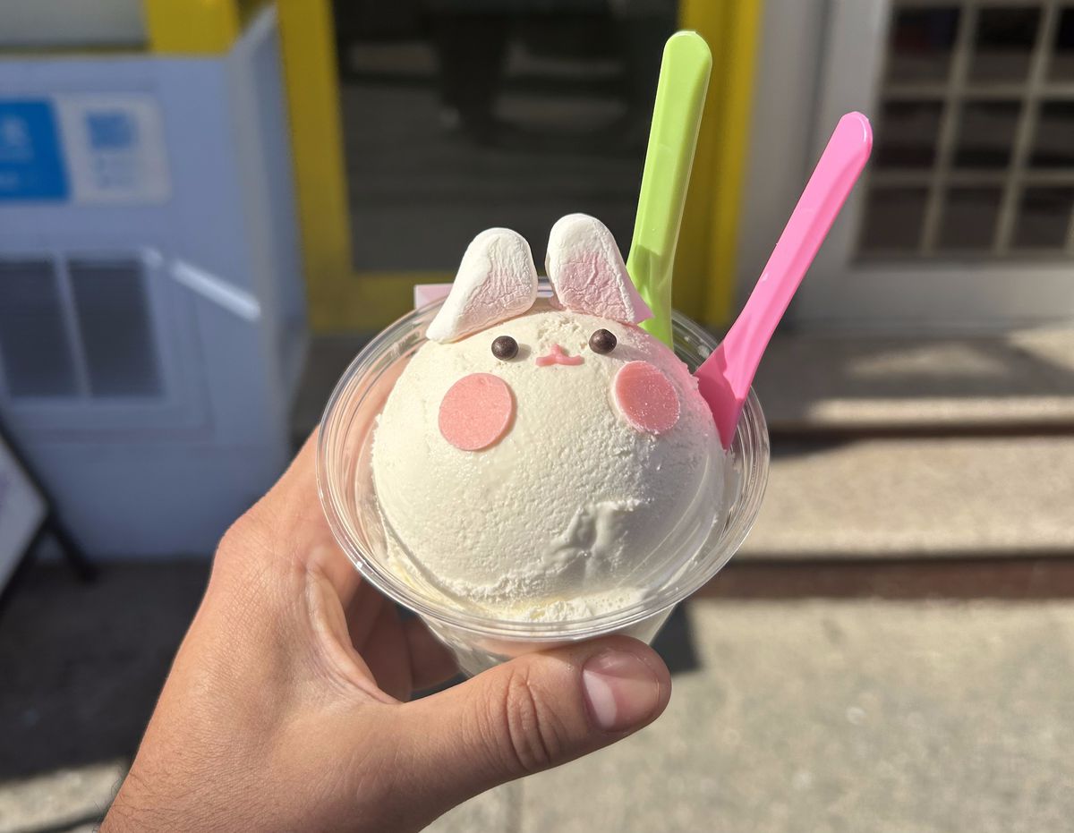 A hand holds a plastic cup with a scoop of ice cream shaped like a bunny.