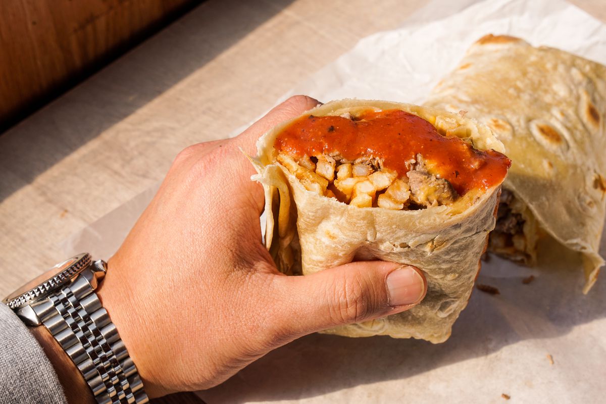 A man holds a half of a burrito with hot sauce. 