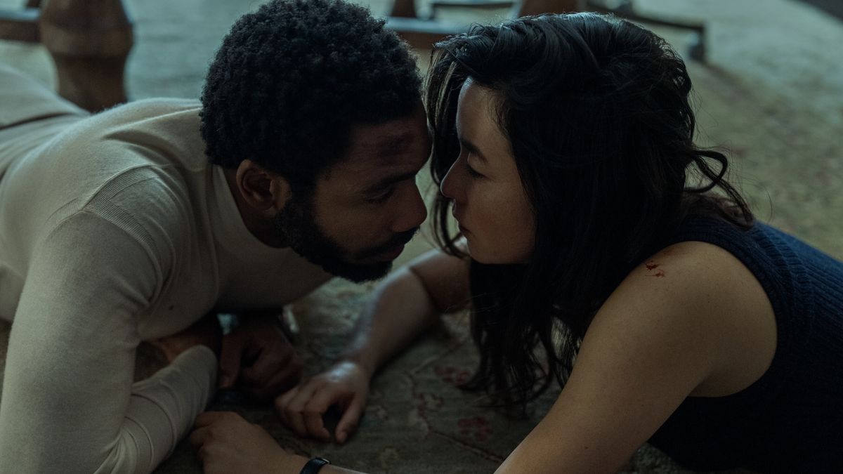 Donald Glover and Maya Erskine, lying on the floor, lean in to kiss in Mr. &amp; Mrs. Smith