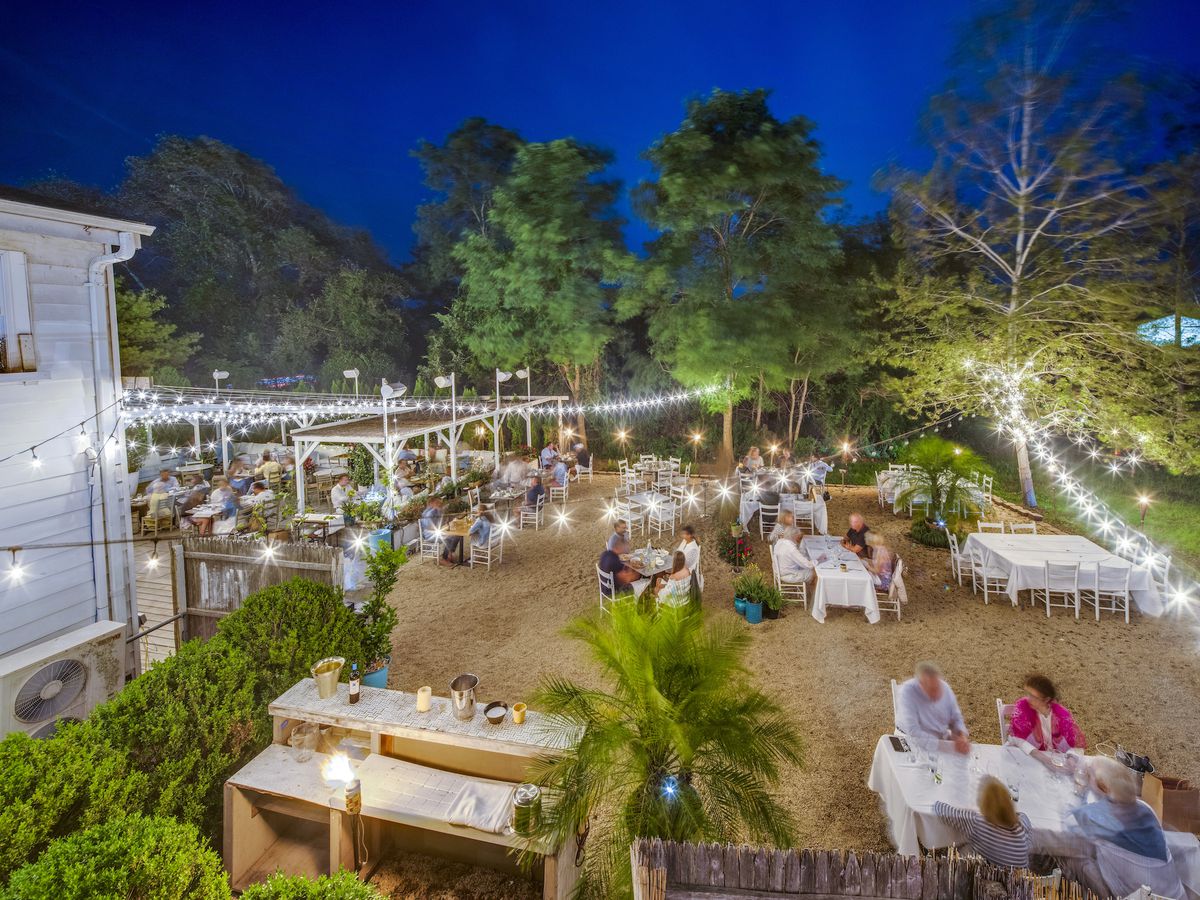 An outdoor dining area with string lights, a few trees, and tables scattered about.