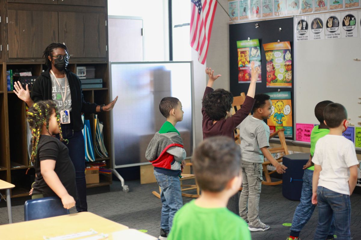 A young teacher dances with her students in their classroom.