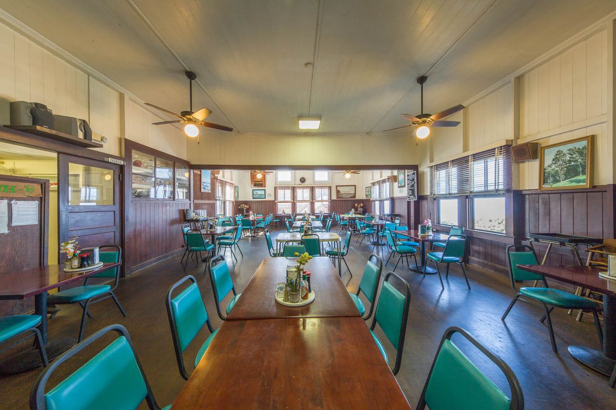 An empty, old fashioned dining room with wood panelling and blue vinyl chairs,