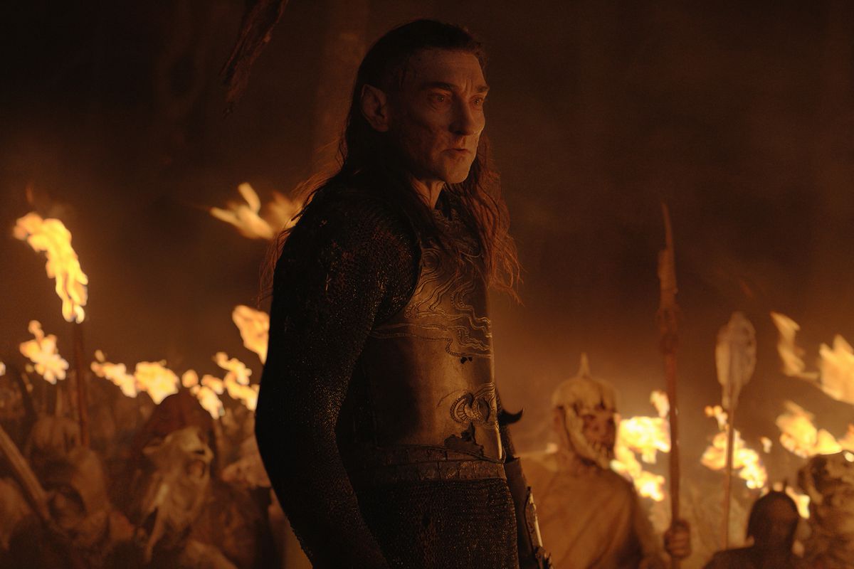 Joseph Mawle as Adar, a scarred elf/orc, standing in front of his orc forces, who brandish torches in the darkness. 