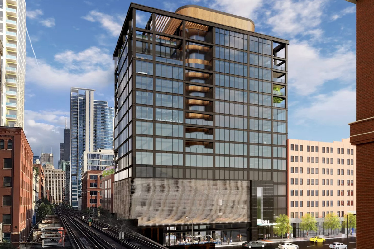 A 15-story office tower rises next to elevated train tracks. The building has a black metal frame with multiple balcony cutouts and an undulating mesh screen at its base. 