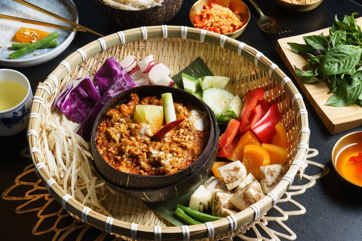 A basket holds an array of chopped vegetables and a small dark bowl with a rich stewy dish inside.