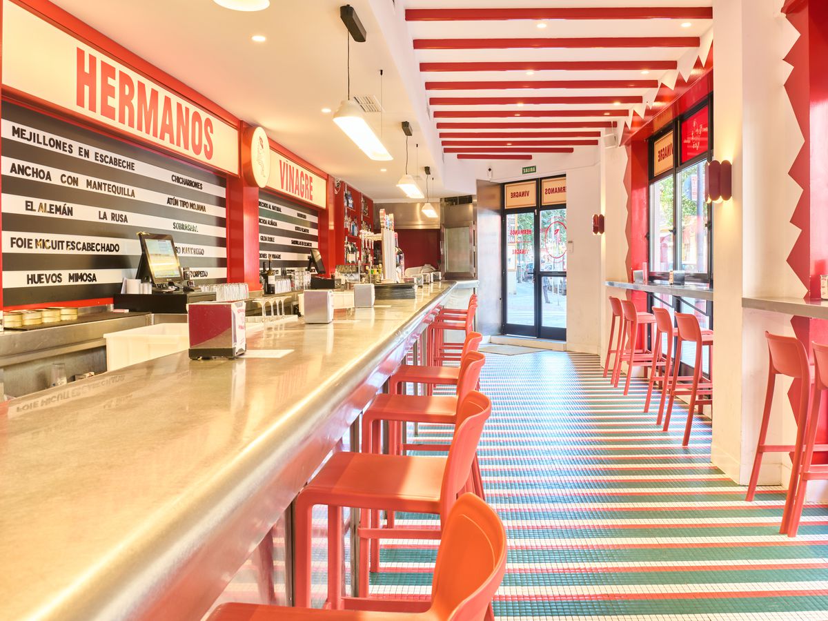 A bright white and red restaurant interior with bright red stools, beamed ceiling, long counter, and large windows.