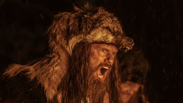 Alexander Skarsgard, vestido con una piel de lobo, aúlla durante un ritual de guerra a la luz del fuego en The Northman