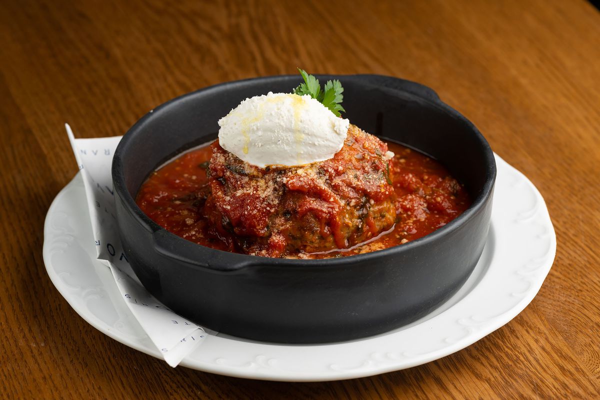 A wide cast iron dish with a sauced meatball and ricotta.