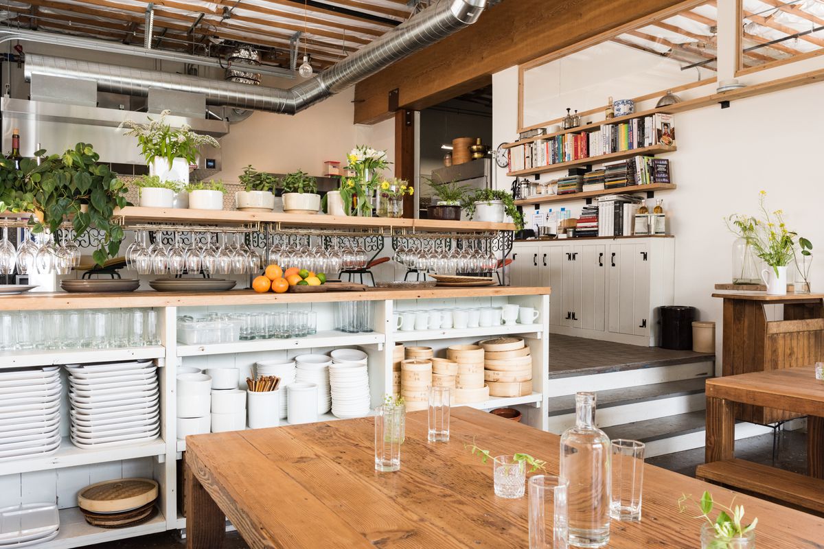 A communal table at Han Oak butts up against a set of built-in shelves next to a staircase, which leads into a small kitchen and chef’s counter.