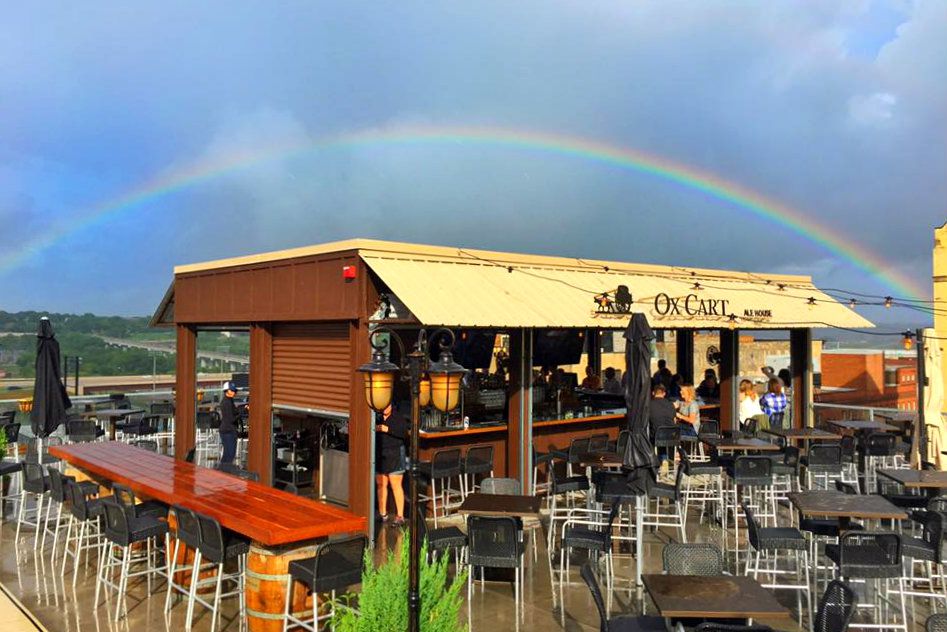 Open rooftop bar with a yellow awning and outdoor seats are all under a rainbow just after a storm