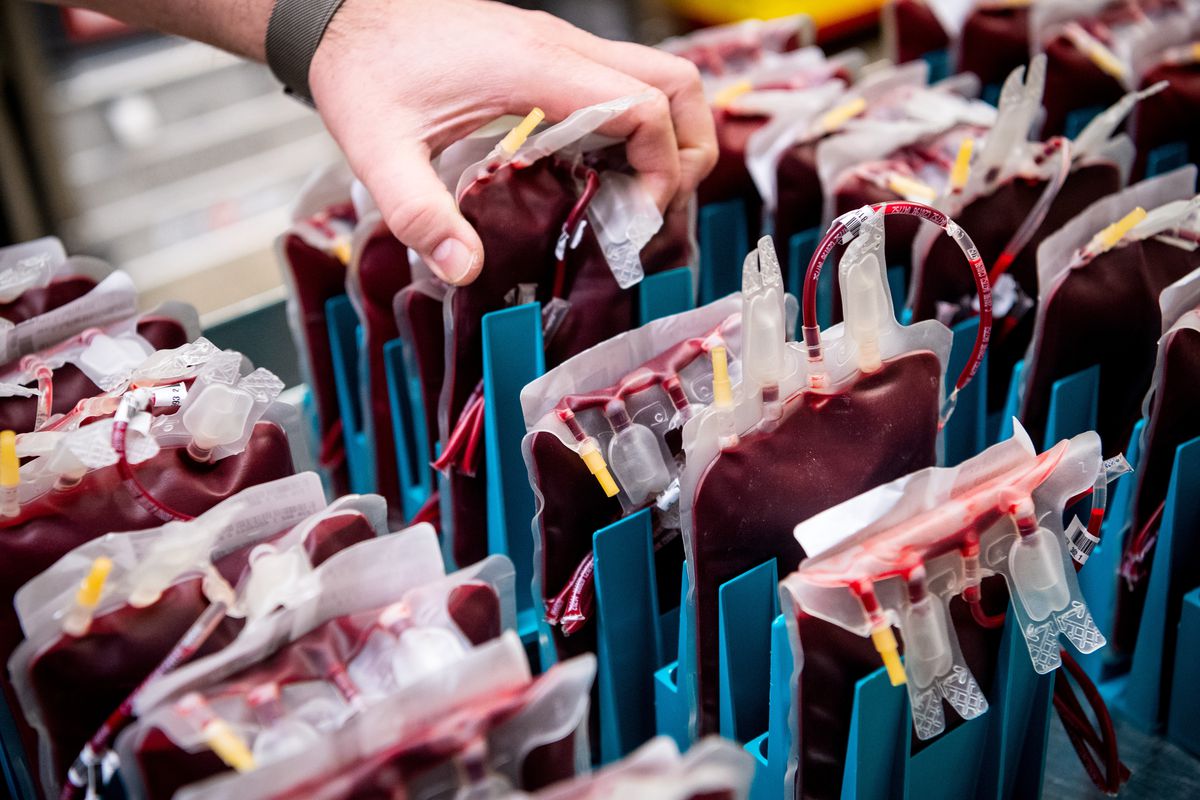 A hand reaches into a storage shelf packed with pouches of donated blood.