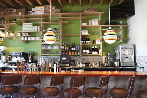 A bar with a lime green background and a lineup of brown stools