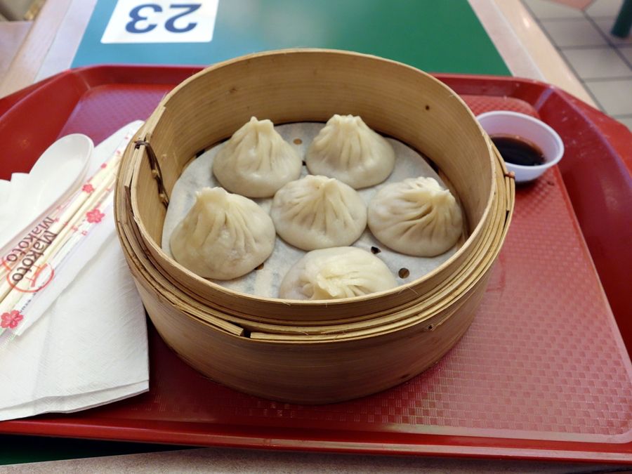 A closeup view of six steamed dumplings inside a wooden vessel.