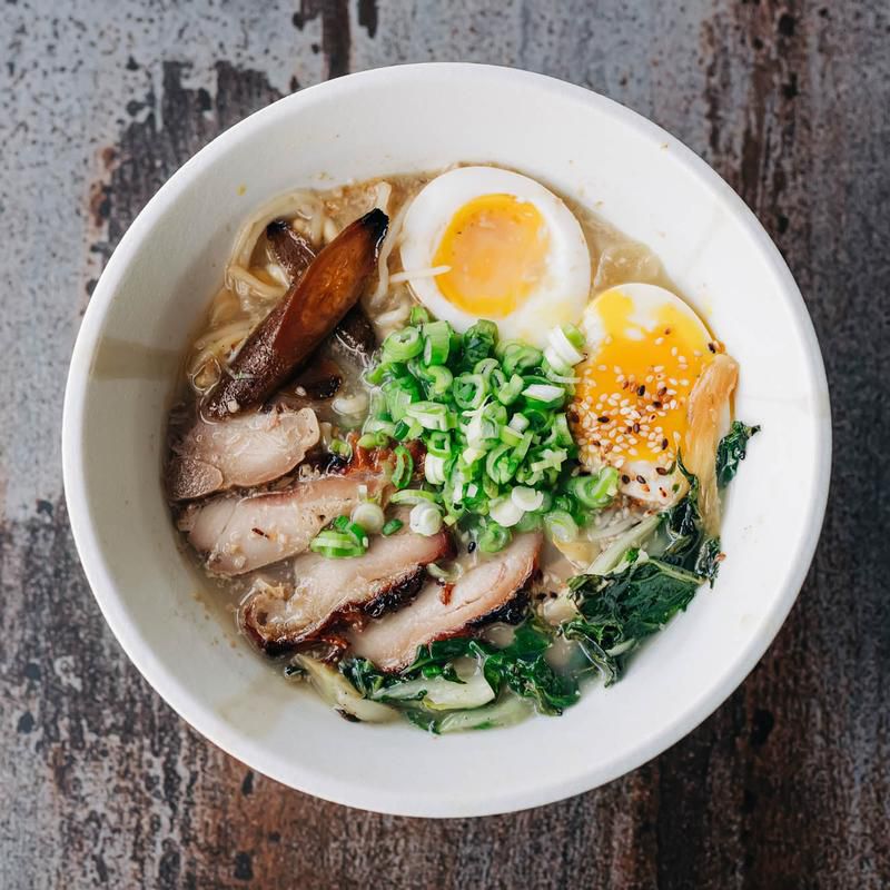 A white bowl of ramen with sliced meat, eggs, and vegetables. 