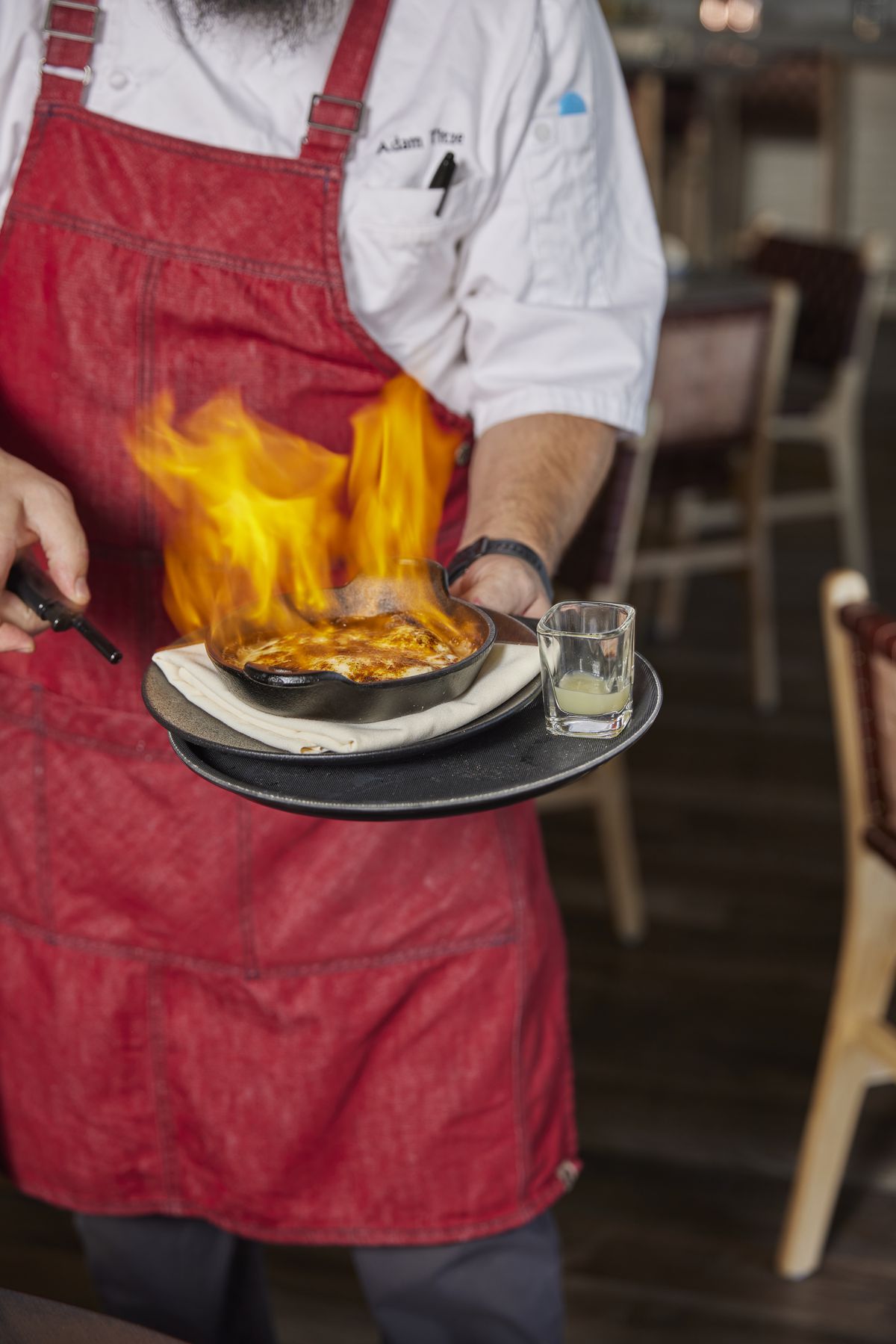 A server walks by with a flaming plate of cheese.