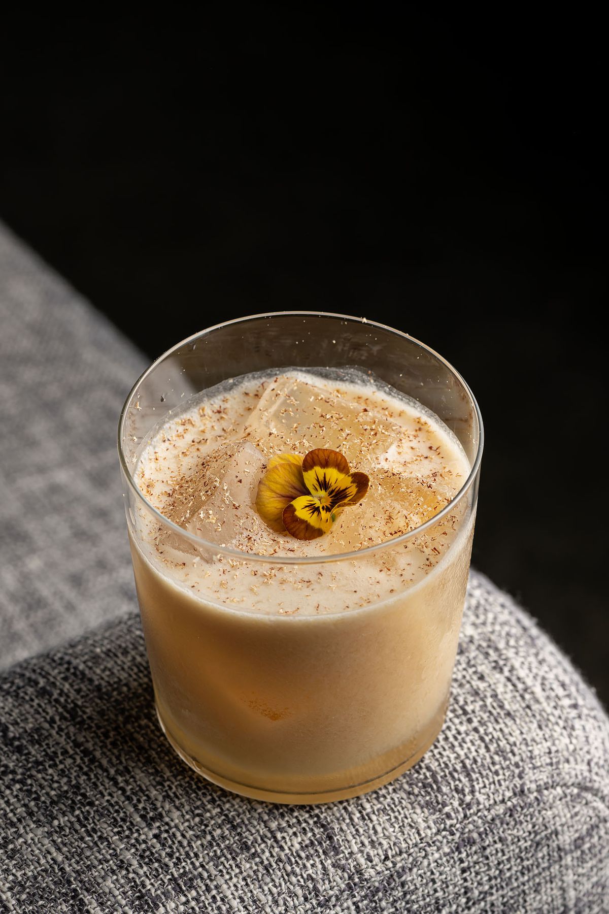 A glass filled with beige liquid with a yellow-brown flower floating on top.