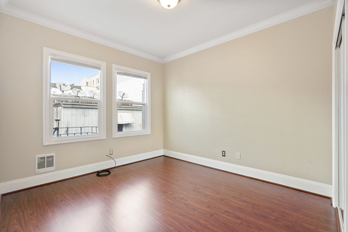 A room with hardwood flooring, two windows with light coming in. 