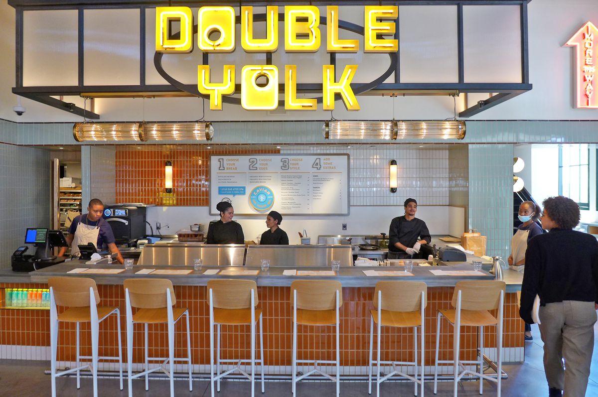 A counter with high stools and a yellow neon sign above.